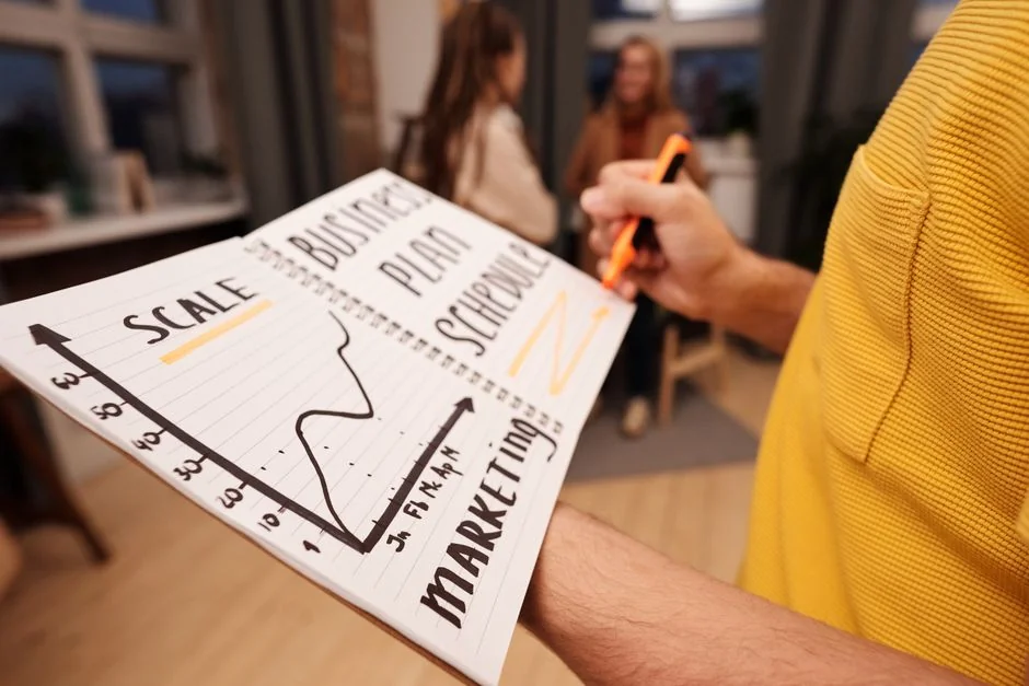 Hands using smartphone trading app with charts, dollar bills in background.